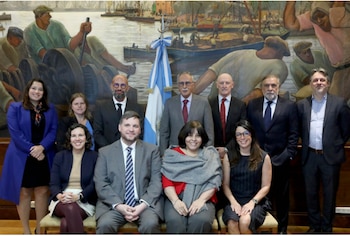 Once personas, ocho hombres y tres mujeres, posando frente a un mural de puerto y la bandera argentina