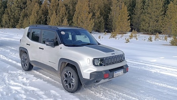 Un Jeep Renegade blanco con techo y detalles negros, estacionado en un camino de nieve, con un bosque de árboles al fondo. Tiene matrícula argentina