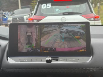 Pantalla digital en el tablero de un automóvil que exhibe la vista de cámaras de asistencia frente a otro vehículo en la vía