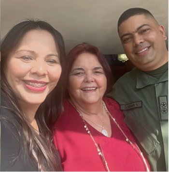 Tres personas posan sonriendo frente a la cámara: dos mujeres y un hombre con uniforme militar verde