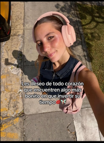 Una mujer se toma una autofoto en la calle con audífonos de color rosa y un bolso, junto a un texto superpuesto en español
