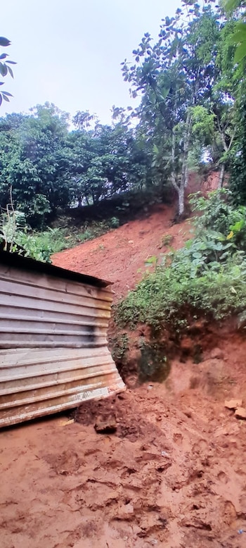 Estructura de metal corrugado parcialmente cubierta por un deslizamiento de tierra rojiza. Ladera empinada con vegetación y árboles verdes al fondo