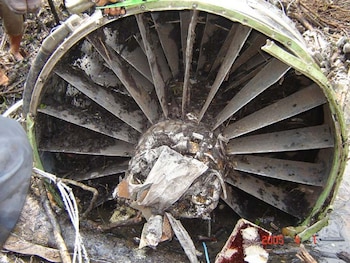 Una turbina de avión con álabes metálicos doblados y cubiertos de barro sobre el suelo