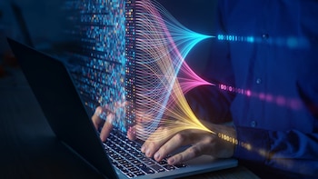 Manos de una persona escribiendo en el teclado de una computadora portátil rodeadas por líneas luminosas y código binario