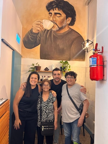 Cuatro personas posan en una cafetería bajo un mural pintado de Diego Maradona bebiendo de una taza