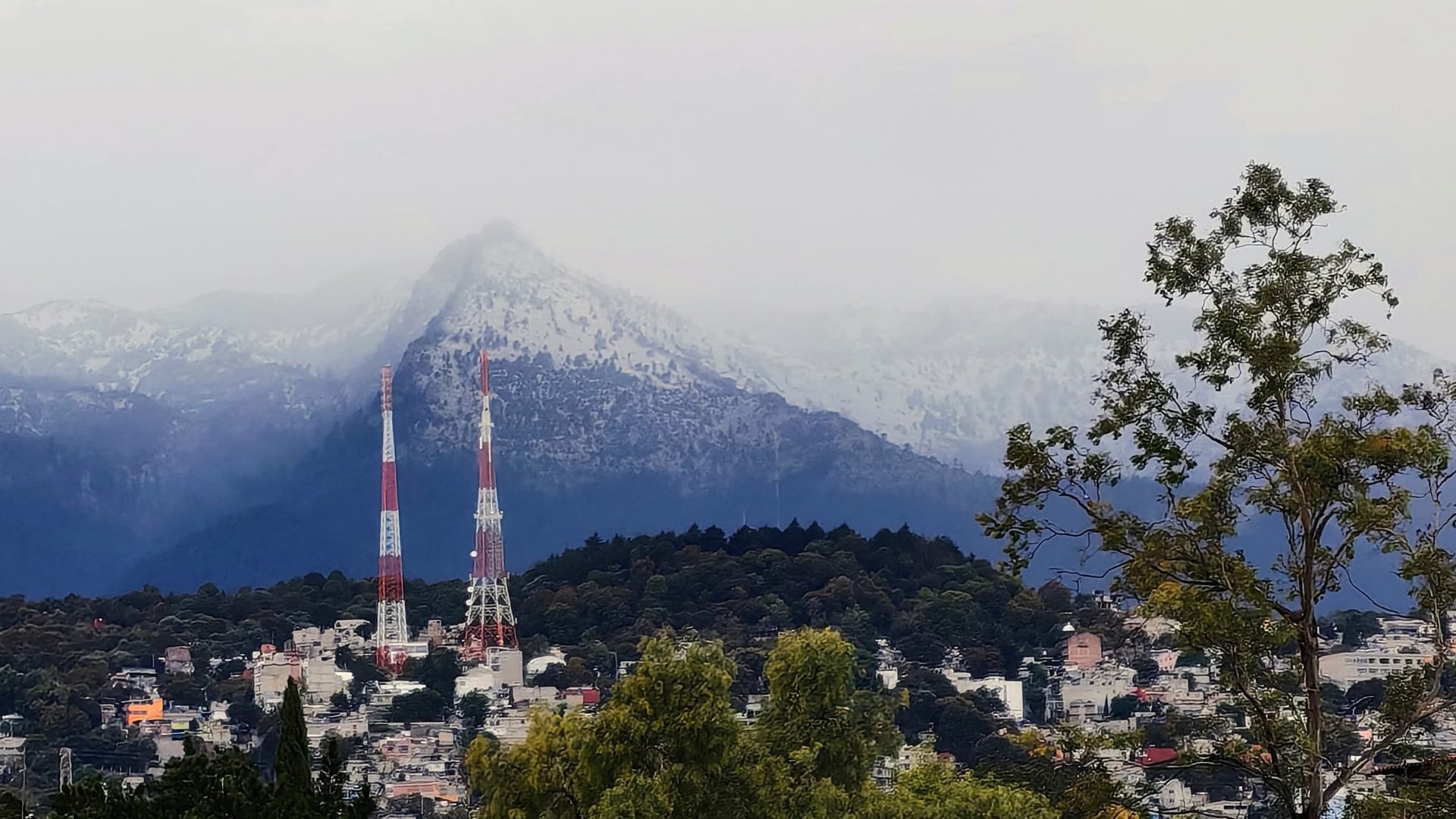 Las emblemáticas cumbres del Popocatépetl e Iztaccíhuatl amanecen cubiertas de nieve tras una nevada atípica de primavera, vista desde una zona urbana cercana. (X/@TlalpanVecinos)
