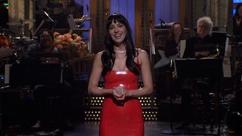 Dakota Johnson sonríe con un vestido rojo sobre un escenario de televisión con músicos al fondo