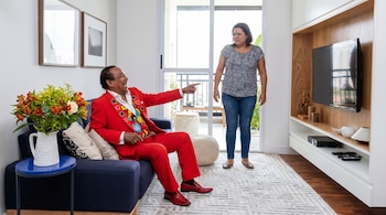 Melcochita, vestido con un traje rojo y camisa estampada, ríe a carcajadas señalando a Monserrat Seminario, quien lo mira con expresión molesta en una sala.