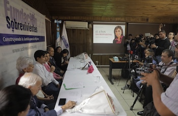Personas sentadas en una mesa y reporteros con cámaras de pie. Detrás, un banner de Fundación Sobrevivientes y una pantalla con una mujer y texto