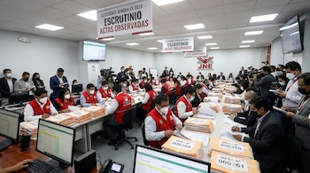 Personas en mesas examinando pilas de actas electorales y monitores. Banners indican 'Escrutinio Actas Observadas Elecciones 2026'. Funcionarios y prensa presentes.