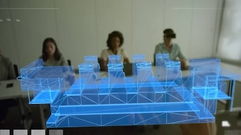 Un modelo 3D azul transparente de una estructura de edificio flota en primer plano, mientras tres personas, una con gafas VR, lo observan