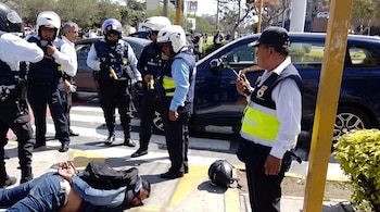 Un hombre yace esposado boca abajo en la vía pública mientras varios agentes de seguridad y policía lo rodean junto a un casco