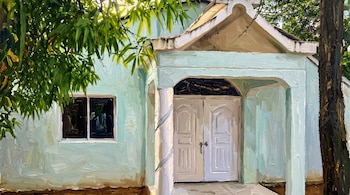 Pintura al óleo de una casa con fachada celeste, puerta doble de madera, ventana y árboles a los lados.