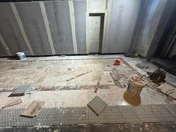 Una estación del Metro CDMX en obras, con el suelo parcialmente cubierto por baldosas de mármol y nuevas baldosas táctiles grises, junto a materiales de construcción y herramientas