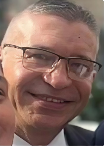 Primer plano de un hombre maduro con gafas de montura oscura, cabello corto canoso y camisa blanca