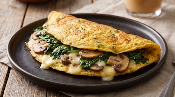 Tortilla dorada rellena de espinacas cocidas, champiñones laminados y queso derretido en un plato negro sobre una mesa de madera.