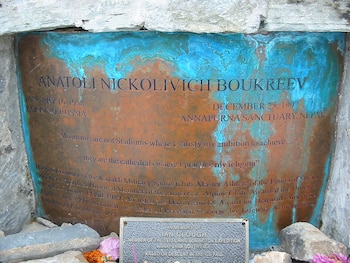 Placa de bronce patinada de Anatoli Boukreev en una pared de roca gris, con texto grabado, fechas y una cita. Debajo, una pequeña placa oscura y rocas en la base