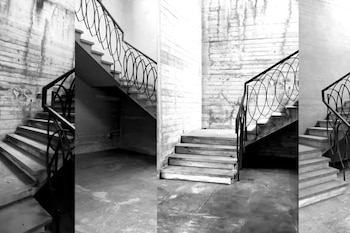 Múltiples vistas fragmentadas en blanco y negro de una escalera con barandilla de hierro forjado y paredes de hormigón texturizado, creando una composición abstracta