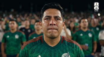 Primer plano de un hombre latino con camiseta verde de México, rostro sudoroso y lágrimas en los ojos, en un estadio nocturno con público desenfocado.