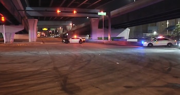 Dos patrullas policiales con luces intermitentes bajo un puente en la noche, con un letrero de calle, marcas de neumáticos y semáforos