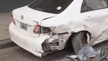 Automóvil blanco con el parachoques roto, la rueda trasera torcida, una óptica destruida y restos de metal sobre el pavimento