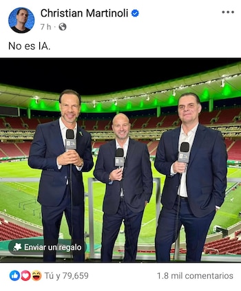 Tres hombres con trajes oscuros posan de pie con micrófonos en un palco de un estadio de fútbol vacío, con asientos rojos y luces verdes en el techo