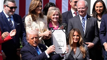 Donald Trump, de traje azul, sostiene un documento enmarcado. A su alrededor, Ted Cruz con gafas de sol, Melania Trump y Maria Elvira Salazar, entre otros funcionarios