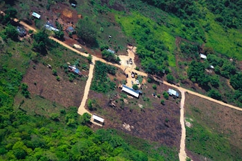 Vista aérea de un paisaje rural con casas de techo metálico y caminos de tierra de color claro. La imagen muestra vegetación densa y áreas deforestadas