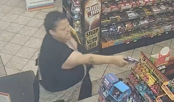 Persona con cabello oscuro y camiseta negra apunta un arma de fuego dentro de una tienda con estantes de productos y suelo de baldosas