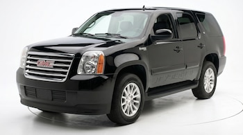 SUV GMC Yukon Hybrid negro brillante visto desde un ángulo frontal y lateral sobre un fondo blanco. Se aprecian la parrilla, los faros, el emblema y las ruedas.