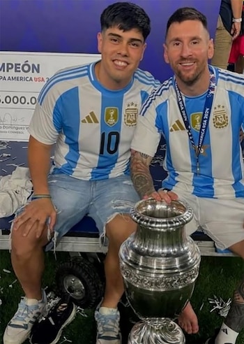Lionel Messi y un joven vestidos con camisetas de la selección argentina posan sonrientes junto al trofeo de la Copa América