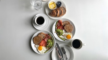 Dos platos con huevos fritos, tocino, aguacate, tomate, espárragos y tostadas. Incluye café, vaso de agua, pan, mantequilla y mermelada.