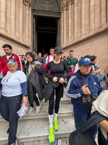 Una mujer vestida con ropa deportiva negra y zapatillas neón baja las escaleras de una iglesia de piedra junto a un grupo de personas