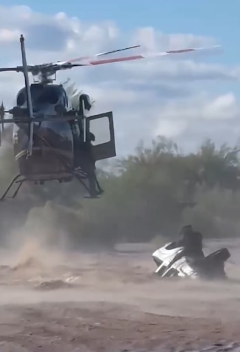 Un helicóptero sobrevuela una zona inundada cerca de una camioneta parcialmente sumergida con una persona sobre ella