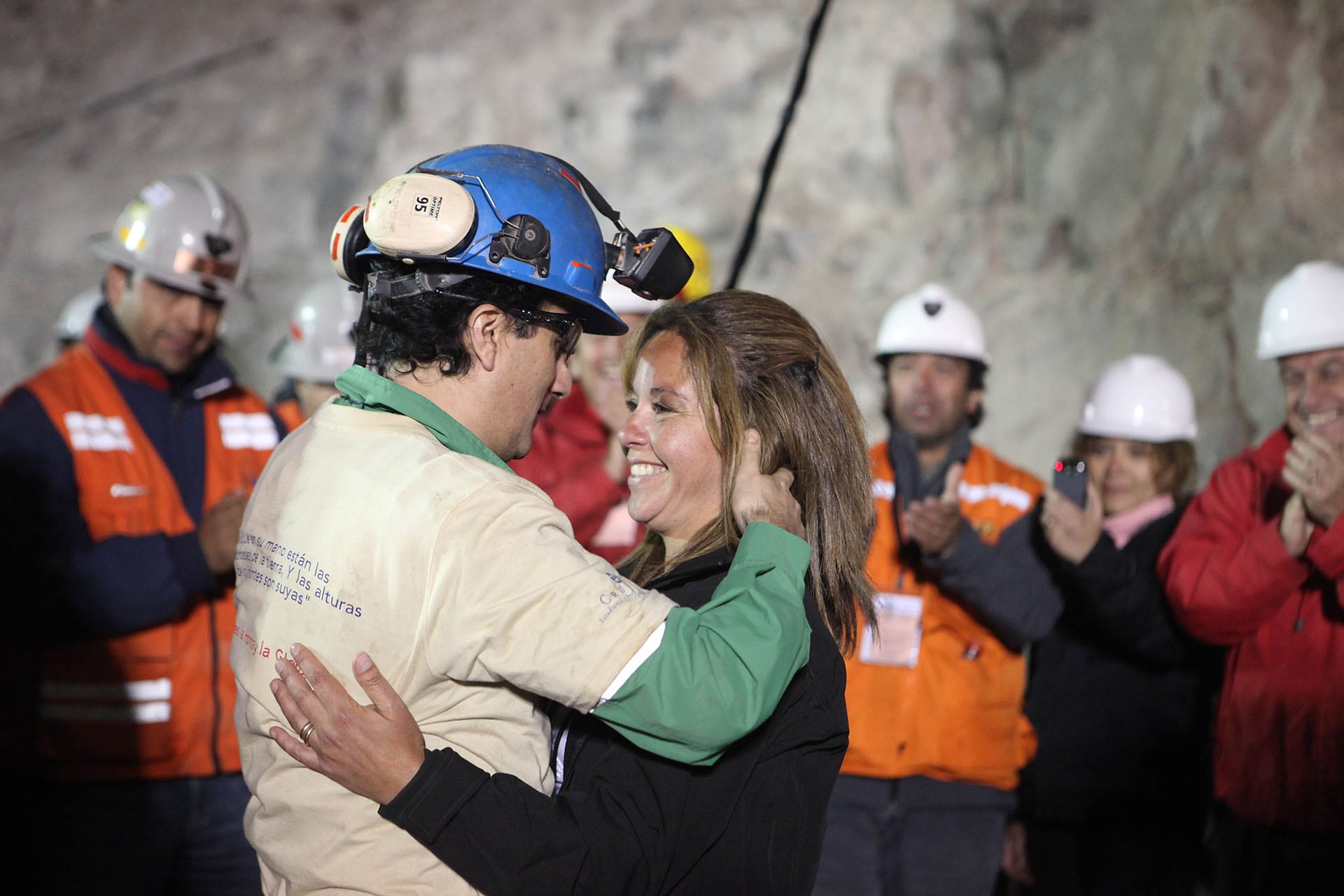 El minero chileno Raúl Bustos abraza a su pareja mientras el presidente de Chile, Sebastián Piñera (derecha), aplaude tras su rescate de la mina San José (Hugo Infante/Gobierno de Chile/AFP)