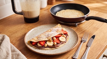 Plato con crepe relleno de crema de chocolate, fresas, rodajas de plátano, avellanas y azúcar glas. Sartén con un crepe, batidora, tenedor, cuchillo, paño.