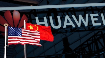 Banderas de Estados Unidos y China sobre mástiles con el logotipo rojo y el letrero de Huawei al fondo.