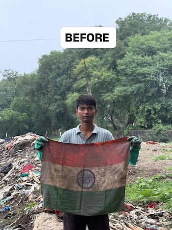 Un joven con guantes verdes sostiene una bandera sucia de la India en un área de desechos con vegetación de fondo y un cartel que dice BEFORE