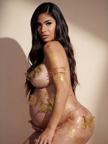 Daniela Celis, embarazada, posa de perfil con el torso desnudo, cubierta de pan de oro y mariposas doradas decorativas, mirando a cámara
