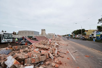 Escombros de ladrillos y estructuras metálicas colapsadas en el borde de una avenida asfaltada junto a un autobús blanco