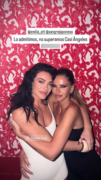 Dos mujeres se abrazan sonrientes frente a una pared decorada con motivos rojos, con etiquetas de texto superpuestas