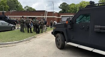 Un grupo de agentes de seguridad y vehículos blindados estacionados frente a un edificio de ladrillo con el letrero Bertie-Martin Regional Jail