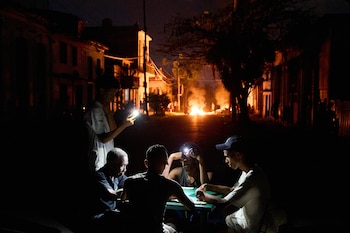 Varias personas se iluminan con sus teléfonos mientras juegan al dominó, al tiempo que arde en una calle de La Habana, Cuba, una hoguera provocada por residentes que protestaban contra los prolongados cortes de luz (Foto AP/Ramón Espinosa)