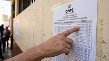 Una mano señala una lista impresa de mesas de sufragio de la ONPE pegada en una pared blanca.
