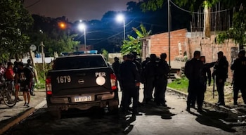 Una camioneta de la policía y varios agentes uniformados de noche en una calle de tierra. Hay personas y viviendas con paredes de ladrillo