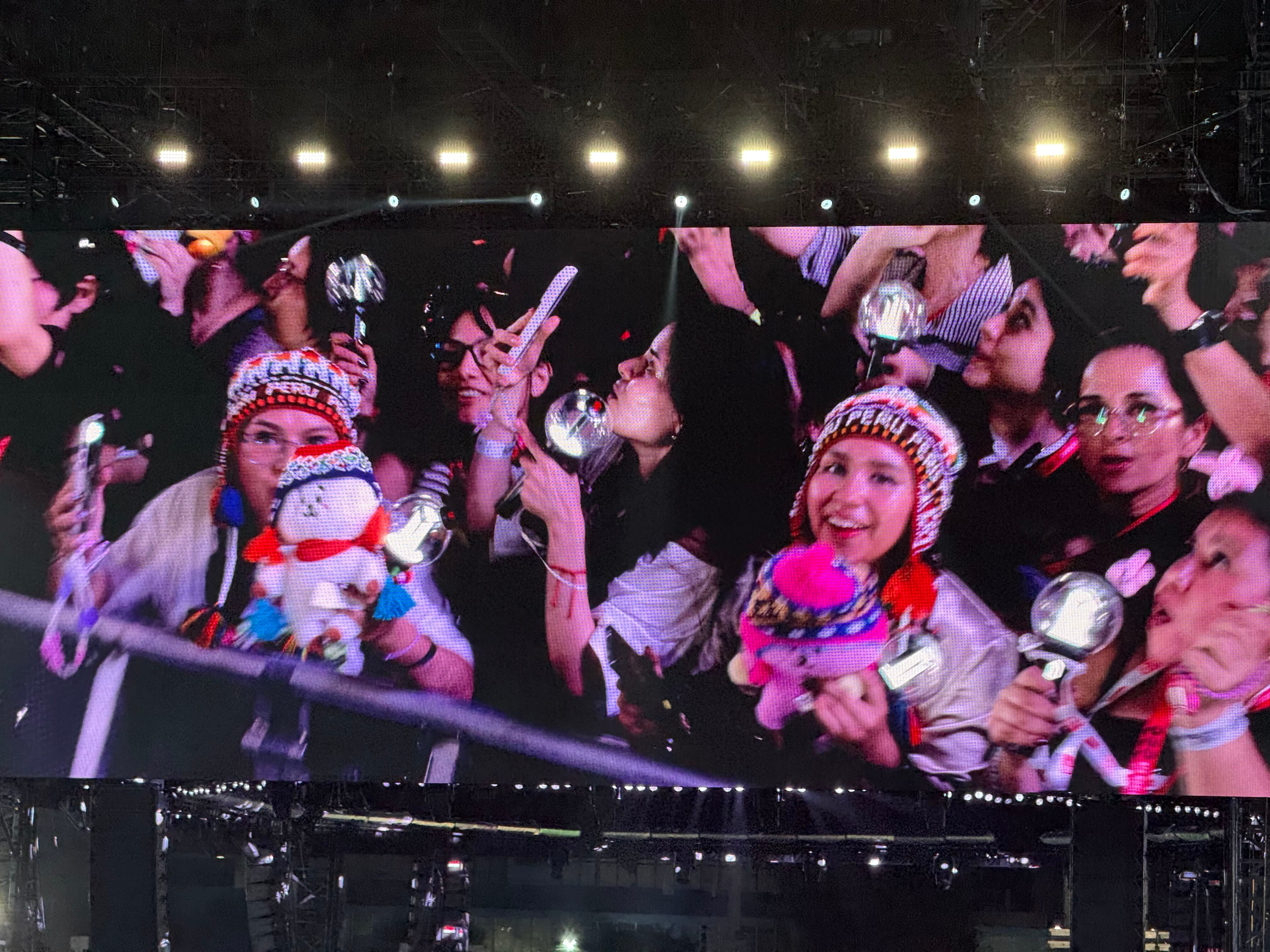 Seguidores del grupo surcoreano BTS celebran durante su concierto en el Estadio San Marcos de Lima con gorros tradicionales y barras de luz. (Paula Diaz)