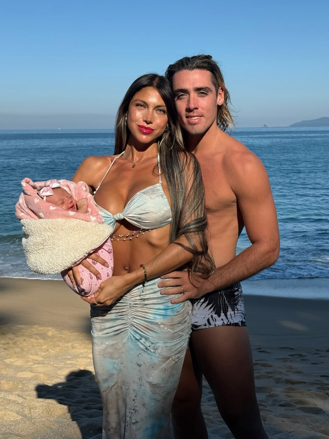 Cielo López y Claudio Spinelli posan junto a su bebé recién nacido en una playa frente al mar.