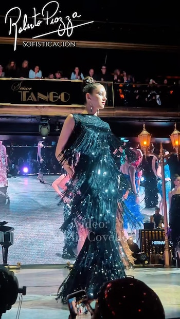 Modelo en pasarela luciendo un vestido largo negro con flecos y lentejuelas de Roberto Piazza, con público y escenario de fondo