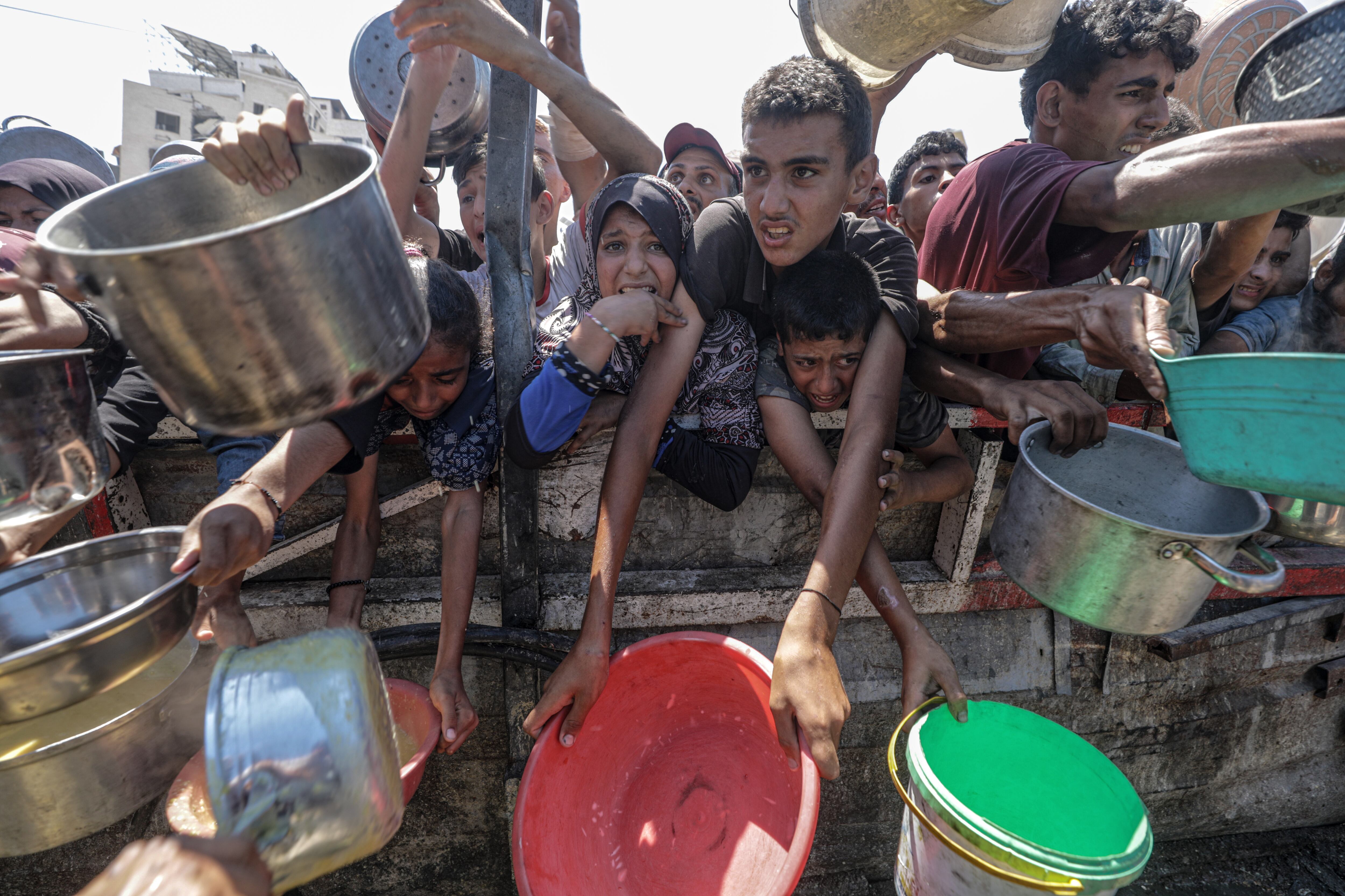 Palestinos desplazados, incluidos niños, con ollas en las manos, mientras esperan recibir comida en una cocina benéfica, en la ciudad de Gaza, Franja de Gaza. (EFE)