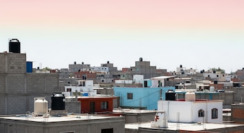 Vista general de múltiples viviendas de concreto y ladrillo con tanques de agua negros y blancos sobre sus techos, bajo un cielo pálido.